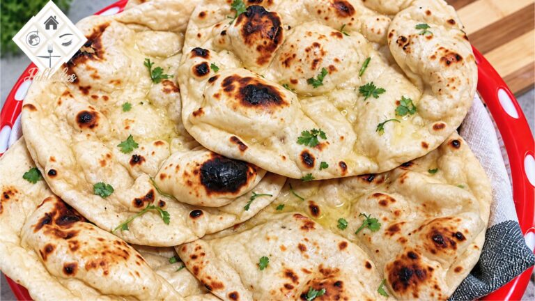 Soft and fluffy homemade tawa naan with golden-brown spots, melted butter and fresh coriander, served on a wooden board.