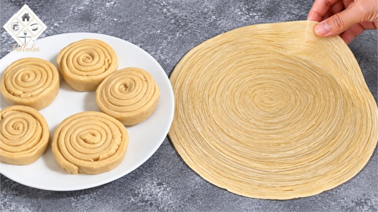 Uncooked Lachha Paratha dough with beautiful spiral layers, five rolled dough portions on a white plate, and a hand lifting the edge of a thin layered paratha to show its flaky texture.